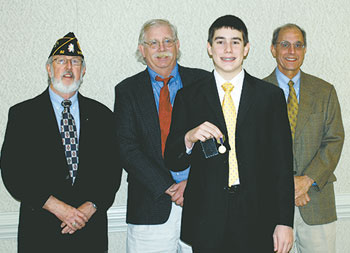 Benjamin  Schaeffer  displays  his  medal  as  officials  Evan  Thompson,  Allan  Nichols,  and  Ali  Paksoy  look  on.