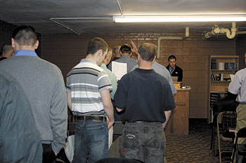 Crossroads Rescue Mission Supervisor Mike Davis asks for prayer requests and then participates with all the men in quoting their eight â€œVerses on Victoryâ€ taken from the Bible. It is part of their daily routine.