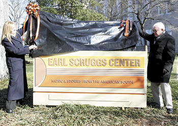 Emily Epley, Executive Director of the Earl Scruggs Center and J. T. Scruggs (nephew of Earl Scruggs) unveil  one of the signs on the court square lawn with its signature "Music & Stories From The American South" theme.