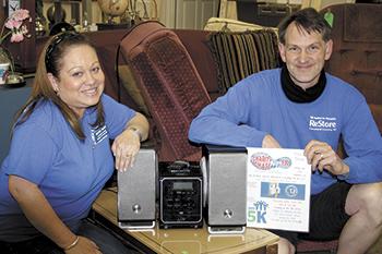 Julissa Black (left)  and ReStore Manager, Scott Mull, show off the iLive CD/radio/iPodDock ($160 Retail) which will be given away to one of the ReStore 5K Runners. In addition 3 clocks ($150 Retail) and 8 Large Backpacks will also be given to runners. 
